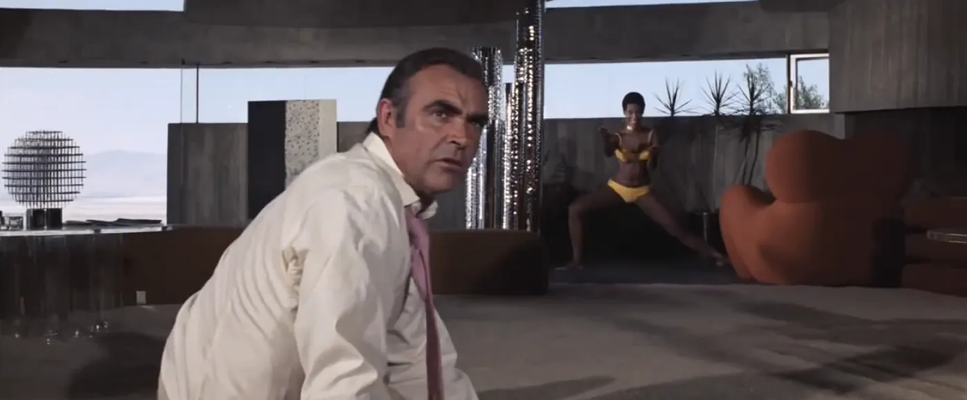 Sean Connery turns warily in a brutalist villain's lair as one of Bambi and Thumper squares up behind him in Diamonds Are Forever