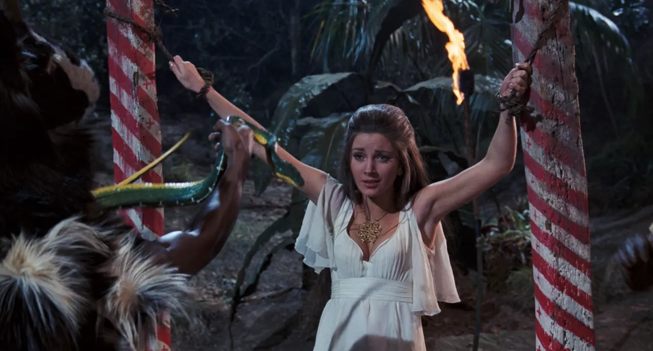 A woman tied to ceremonial posts while a snake is thrust at her during a voodoo ritual in Live and Let Die