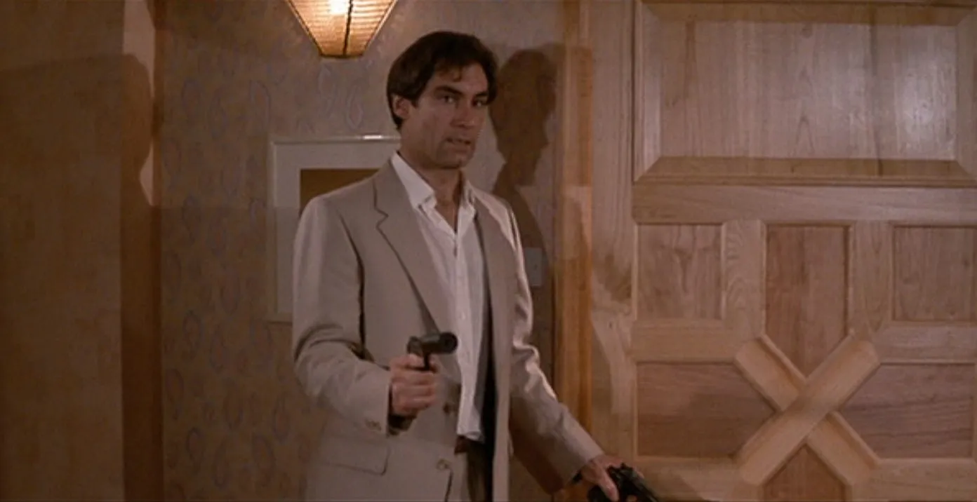 Timothy Dalton as Bond, brandishing a gun in a beige-on-beige hallway in The Living Daylights