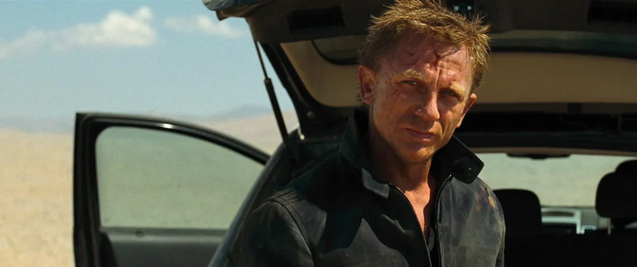 A battered Daniel Craig leans against a car in the desert, looking characteristically worse for wear in Quantum of Solace